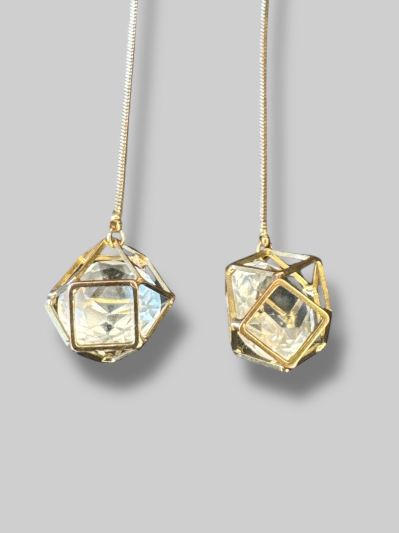 Gold tone dangly geometric cage earrings with faux clear gem inside