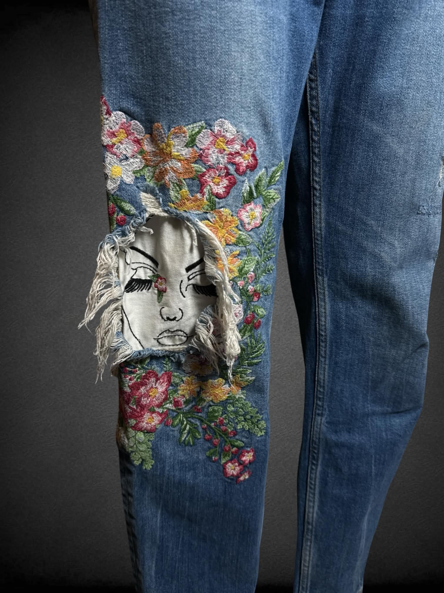 L Zara blue distressed jeans with embroidered floral design, and cutout of a face on knee