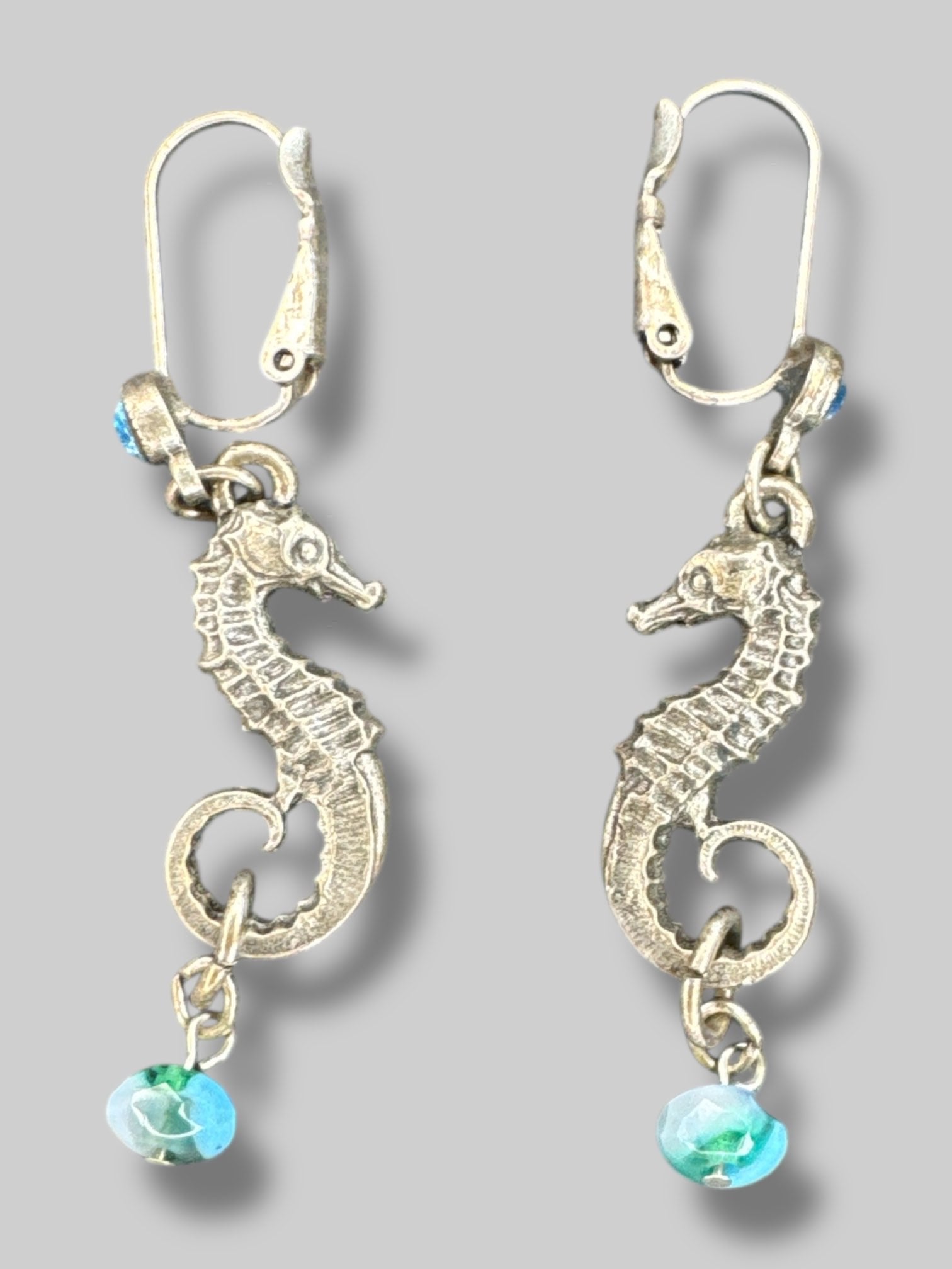 Silvertone seahorse dangle earrings with blue bead on bottom and blue gem on clasp closure