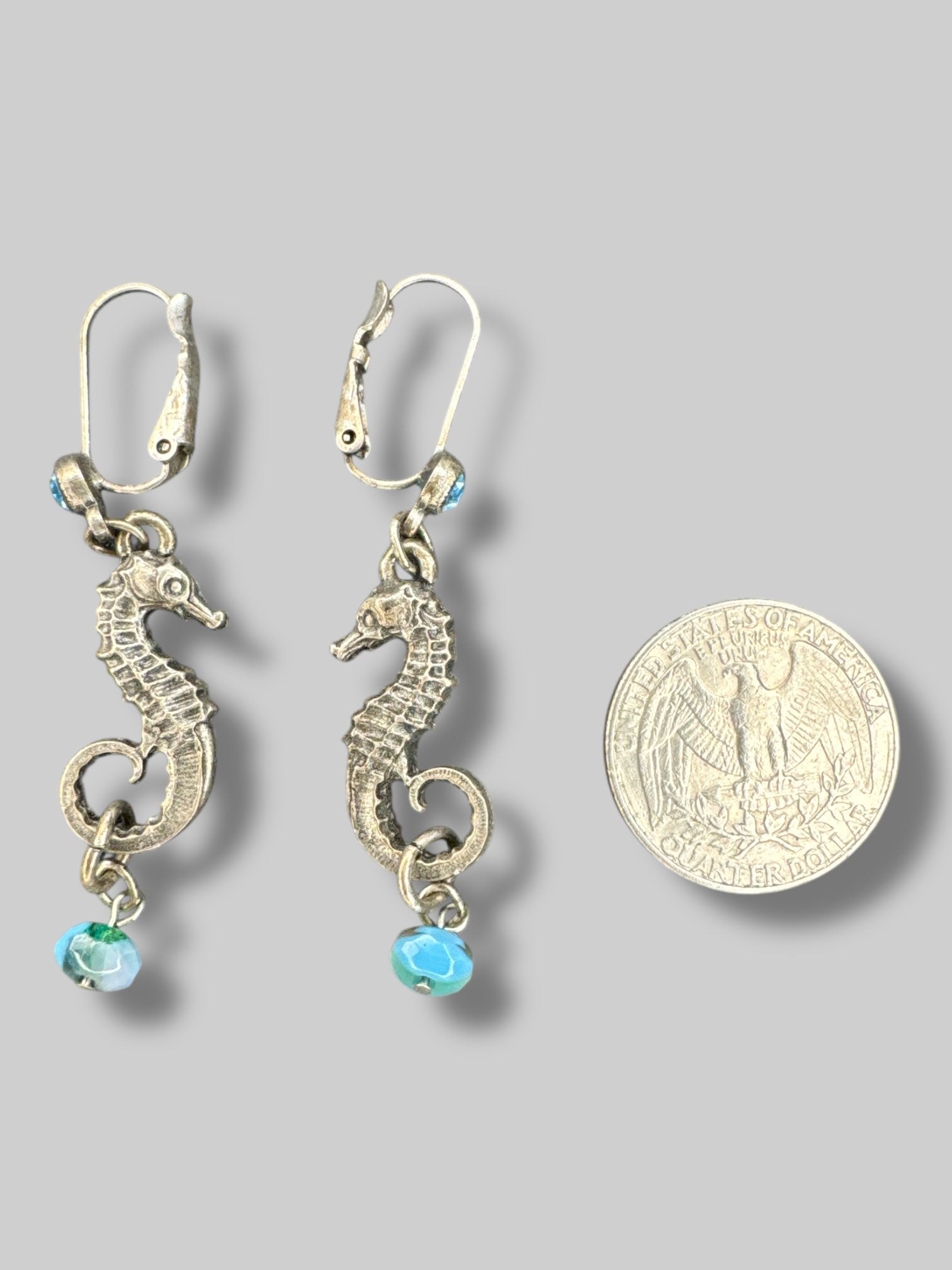 Silvertone seahorse dangle earrings with blue bead on bottom and blue gem on clasp closure