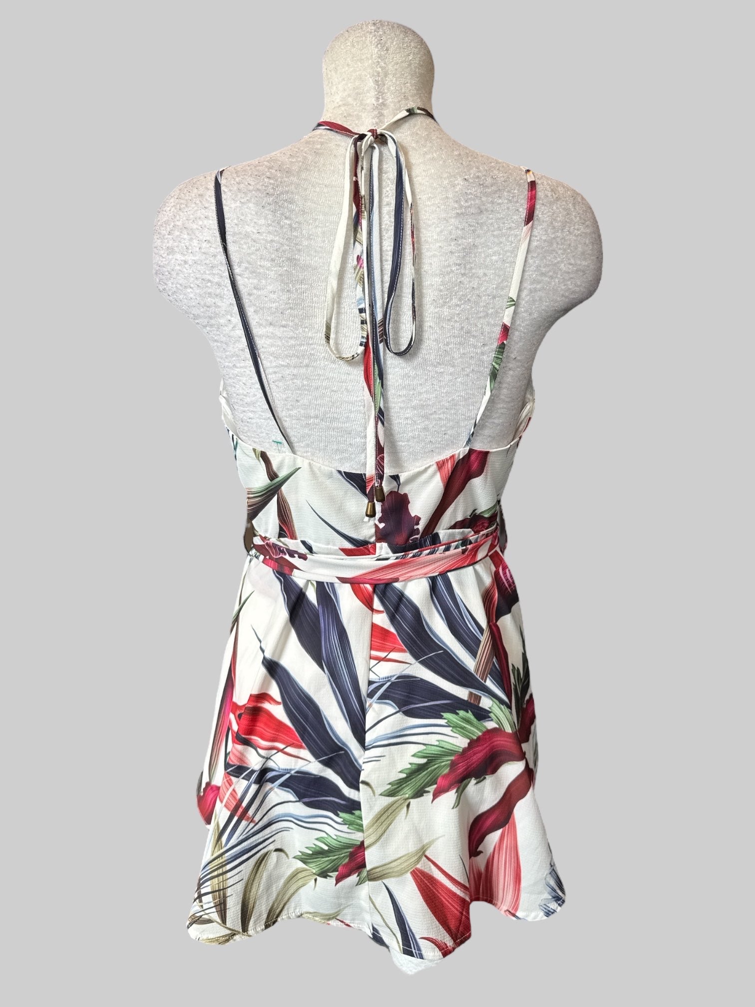 M White sleeveless floral romper with faux wrap design, tie belt, adjustable straps with tie, and zipper on back