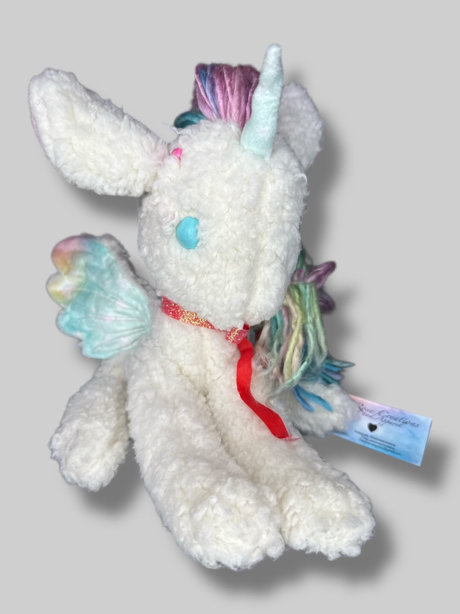 White fluffy unicorn plush with rainbow hair, and wings