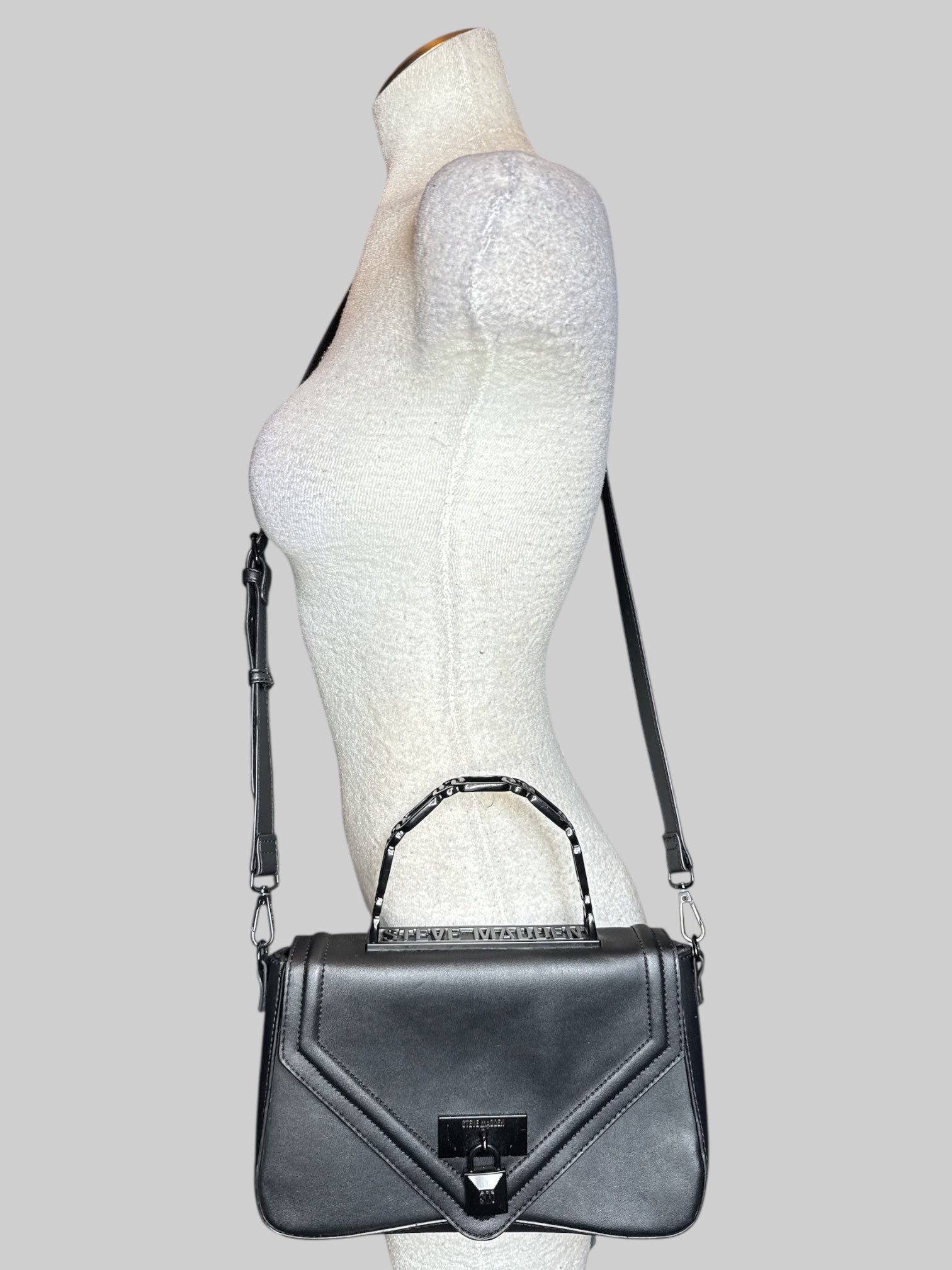 Black leather Steve Madden handbag with hard handle, shoulder strap, faux lock on front, and snap closure