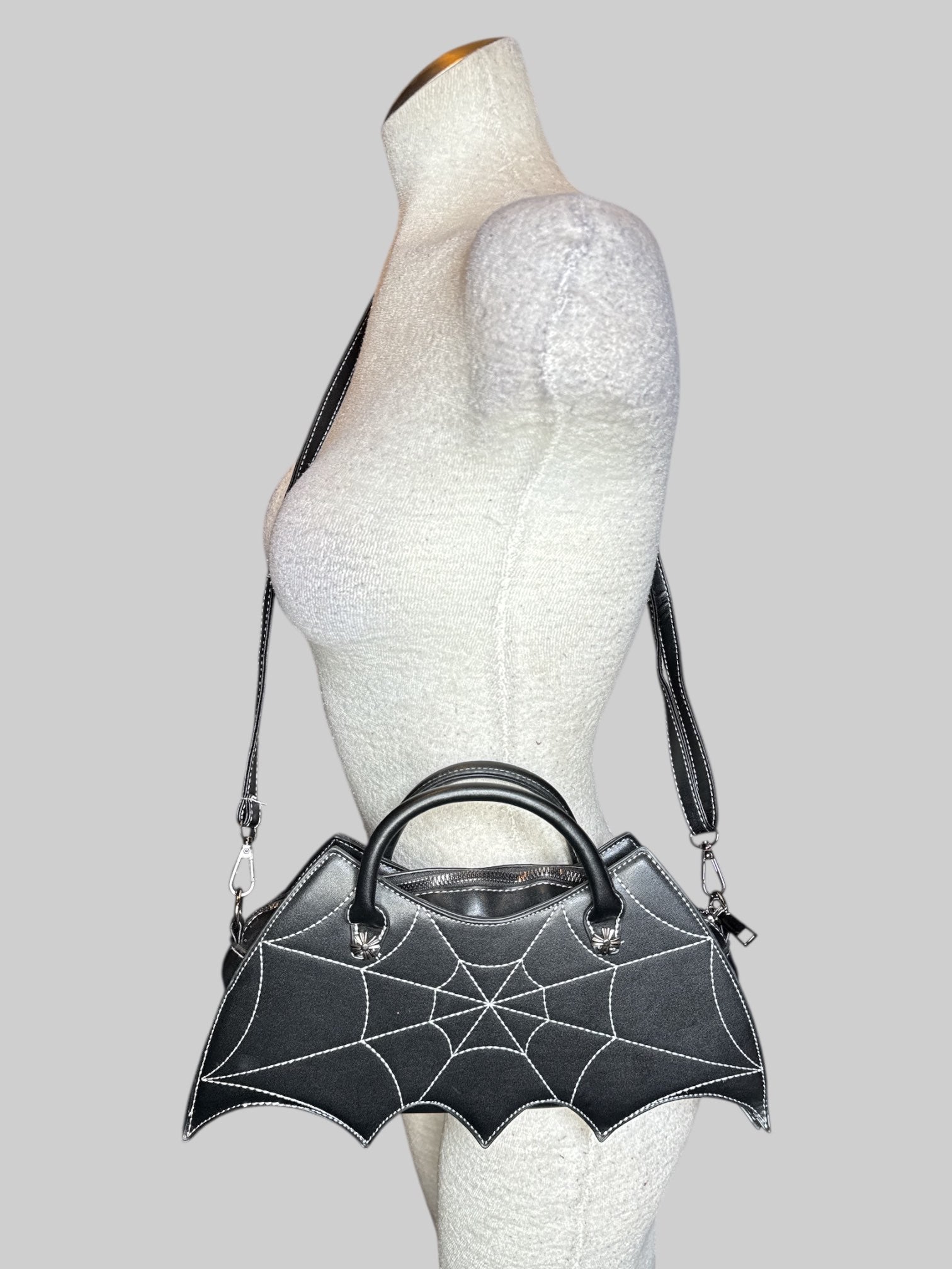 Black leather bat shaped handbag with spiderweb embroidery on front, an adjustable shoulder strap