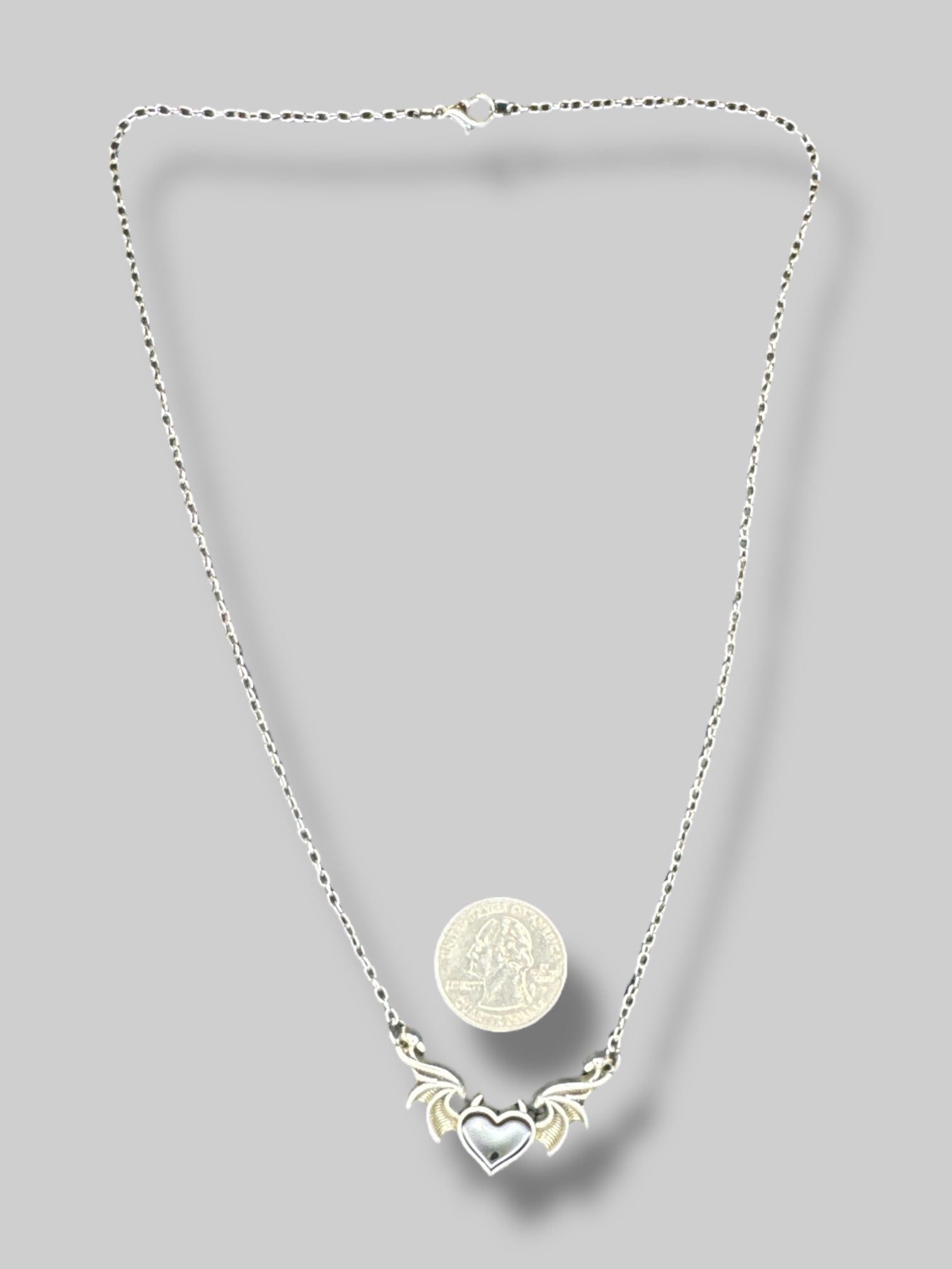 Silver tone necklace with wings and black heart