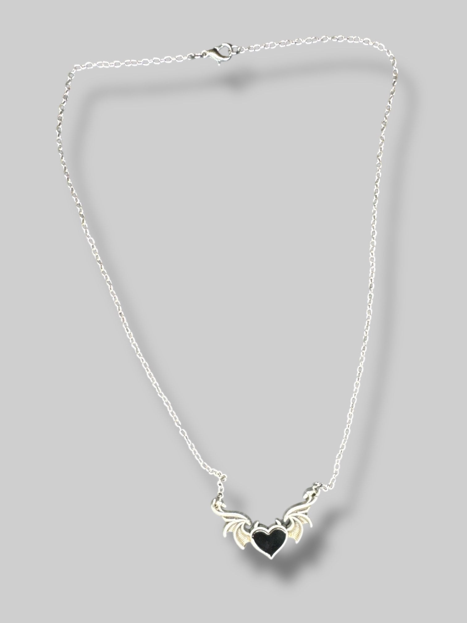 Silver tone necklace with wings and black heart