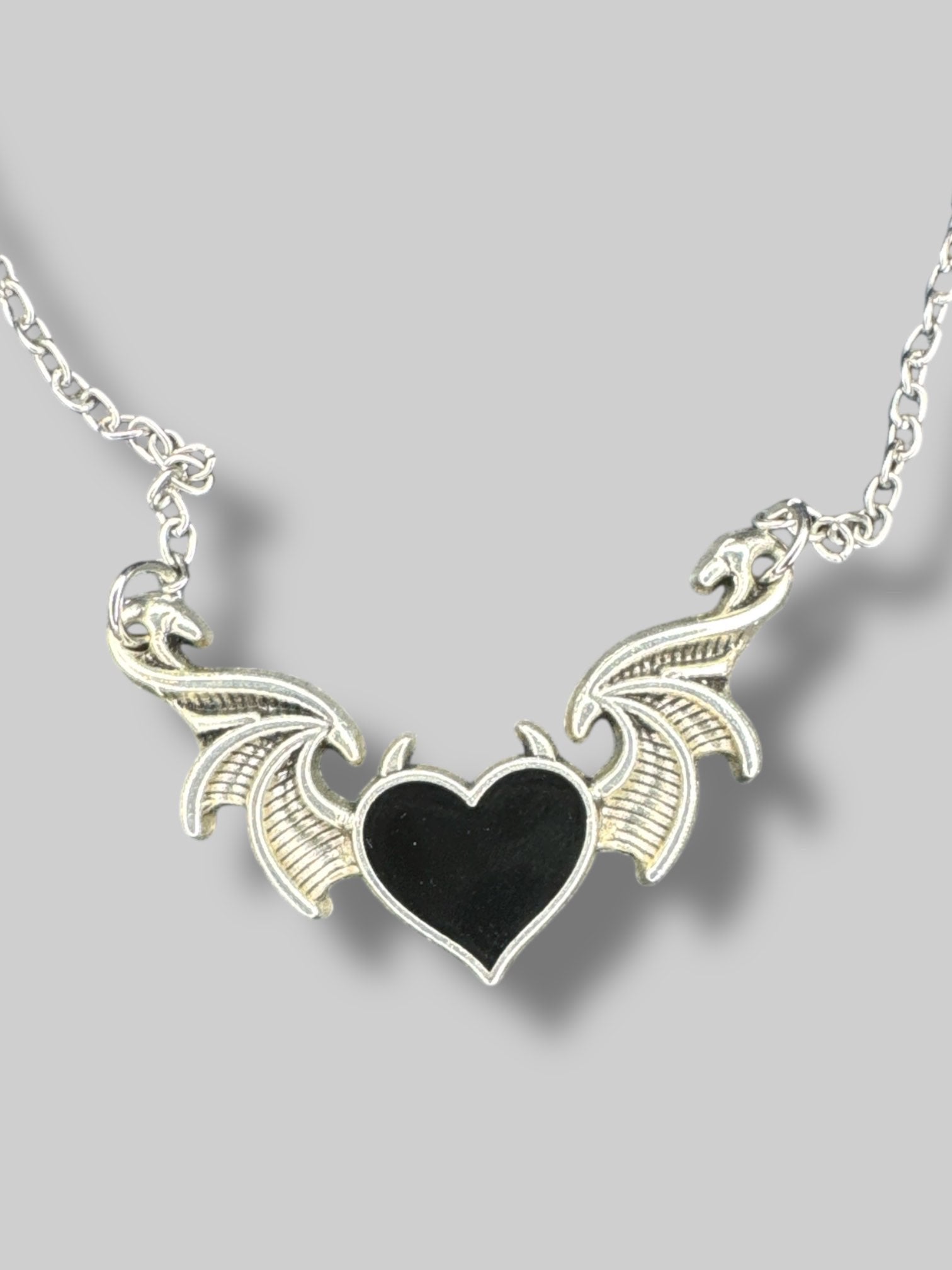 Silver tone necklace with wings and black heart