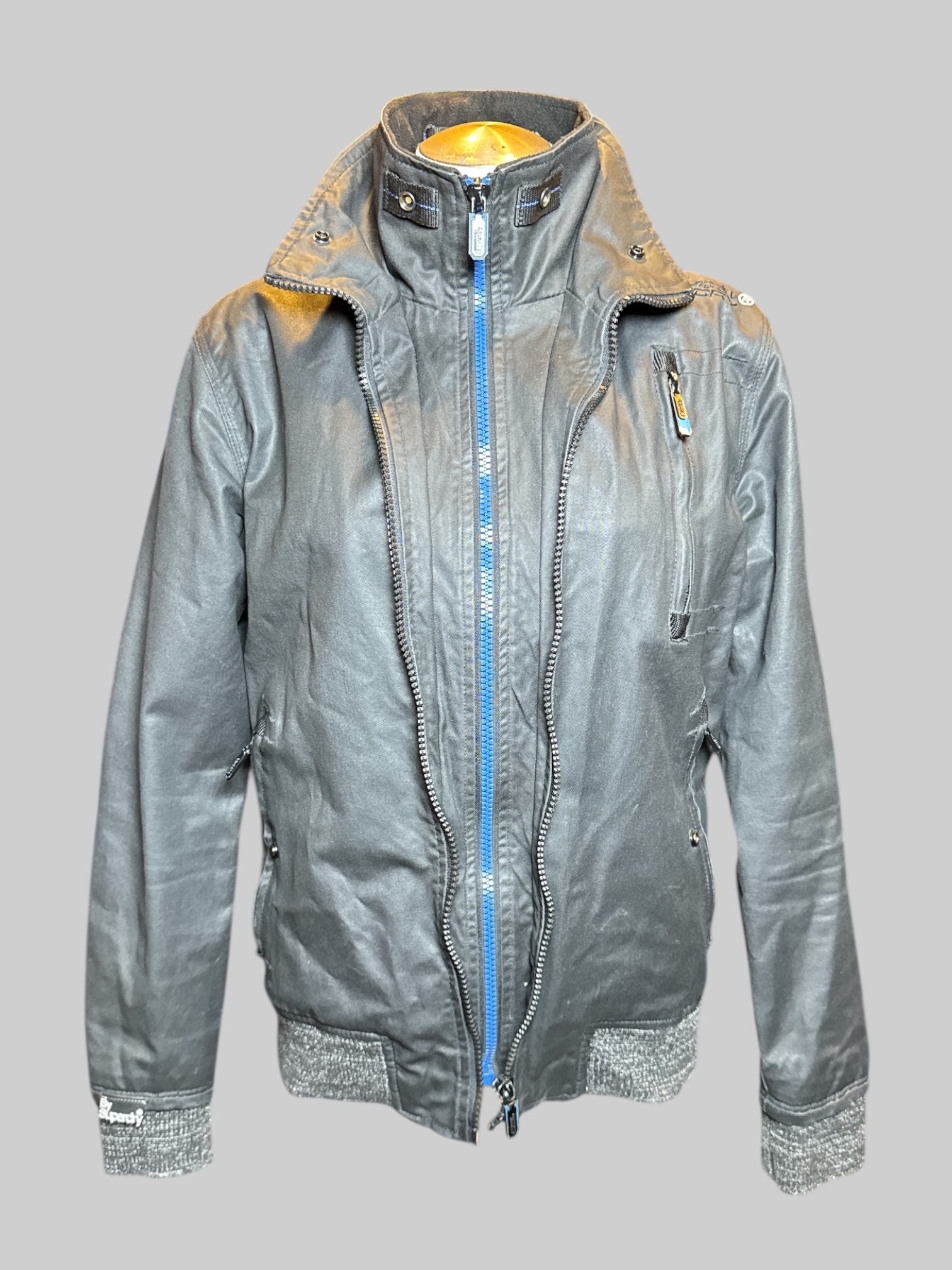 S Superdry black fleece lined zip up jacket with blue accents, zipper pockets, and multiple snap buttons