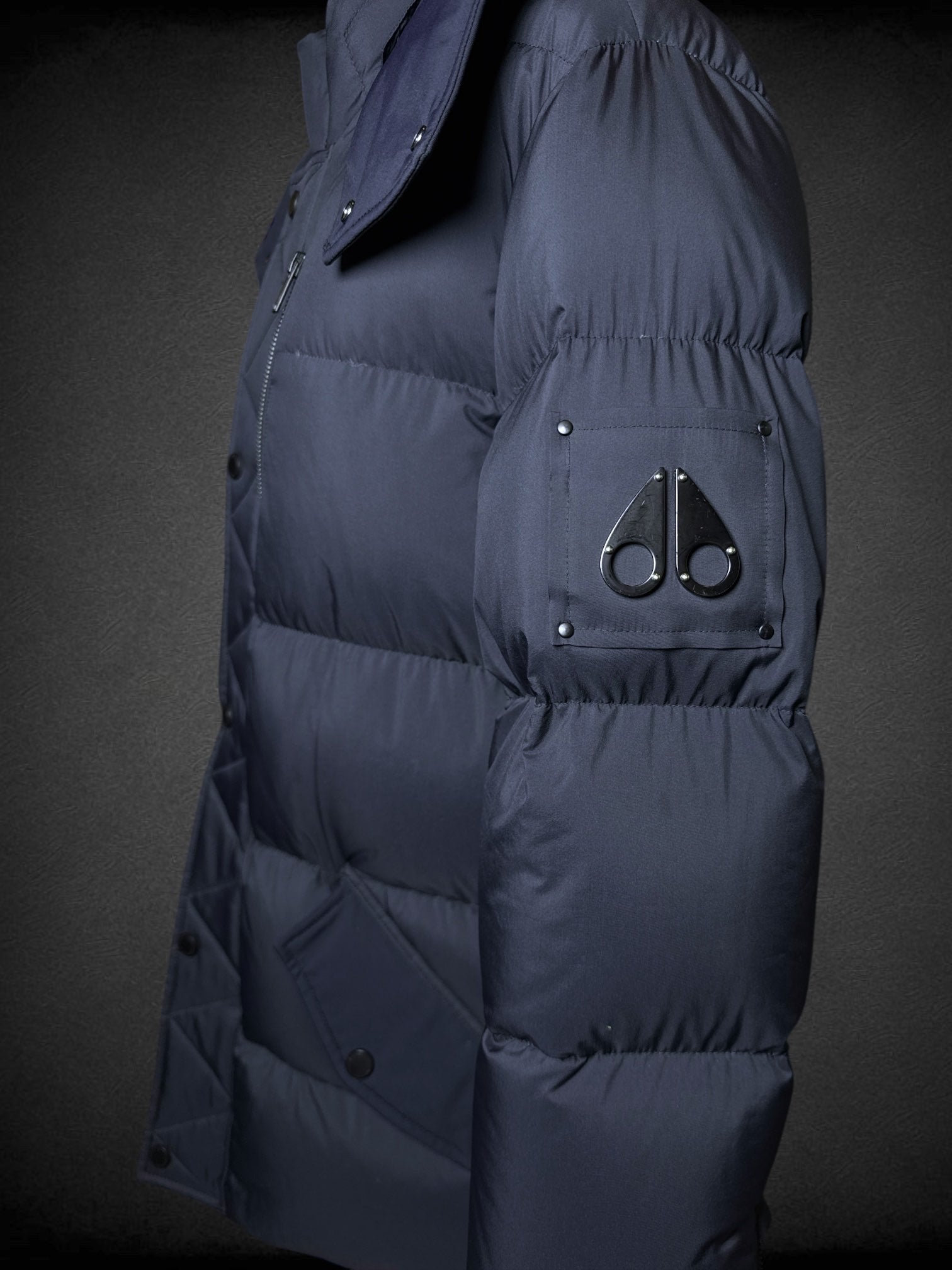 L Moose Knuckles dark blue puffer coat with zipper and snap button pockets, decorative slipper shaped like axe, and logo on sleeve