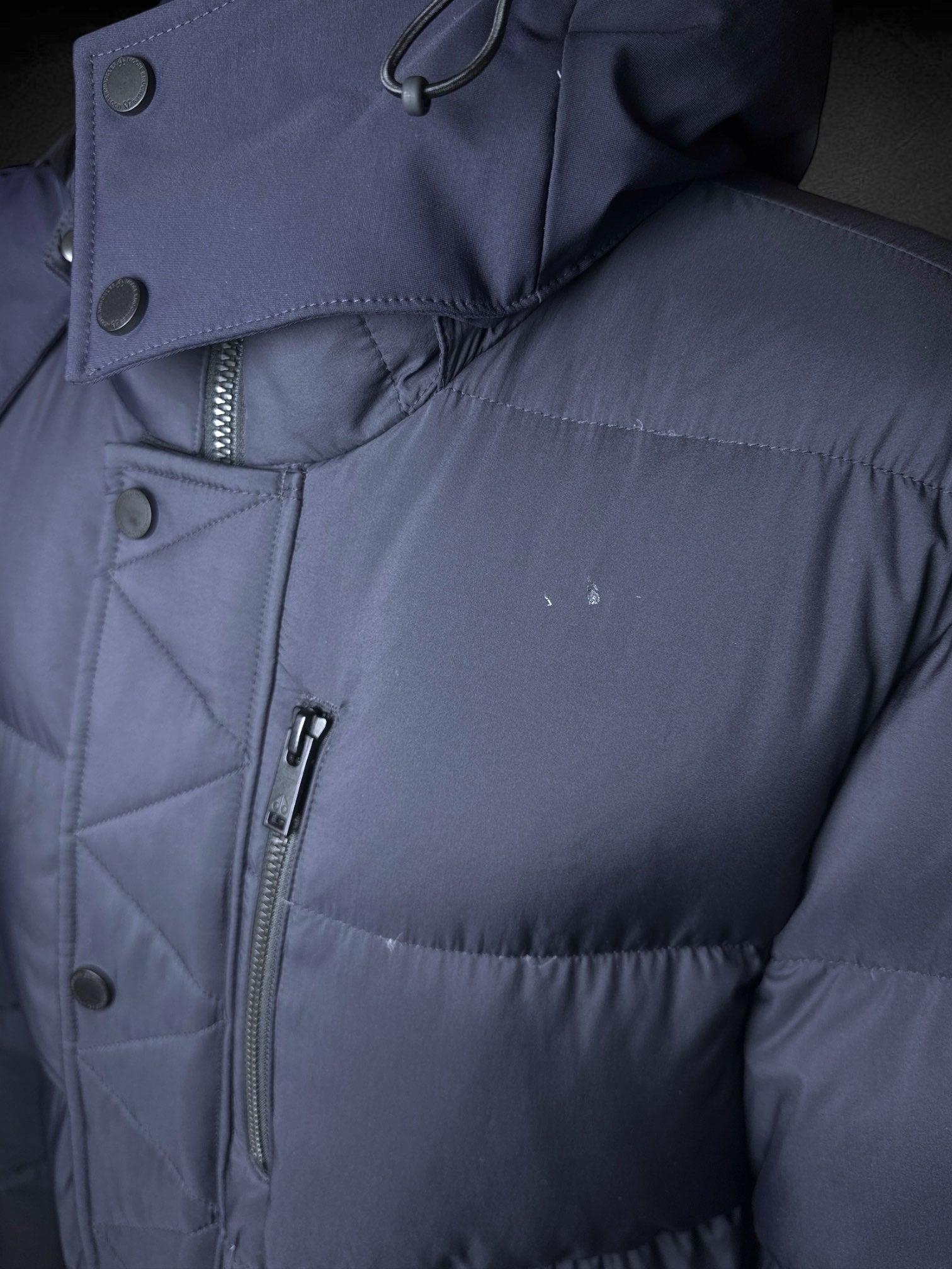 L Moose Knuckles dark blue puffer coat with zipper and snap button pockets, decorative slipper shaped like axe, and logo on sleeve