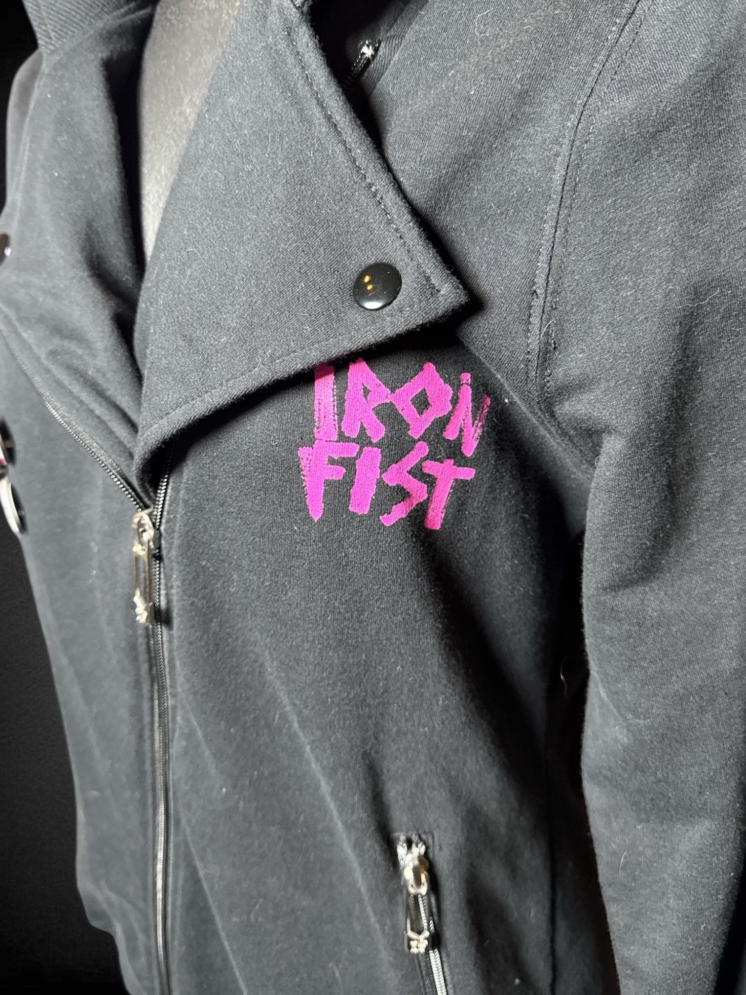 L Iron Fist black long sleeve zip up jacket with pink mohawk punk graphic, and British pins on front