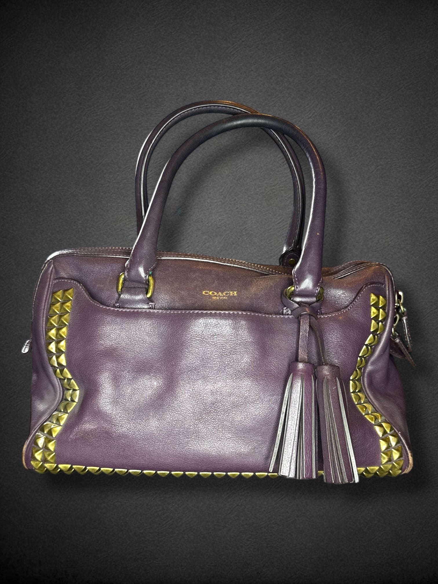 Coach purple leather purse with handles, bronze studding, and large leather tassels on front