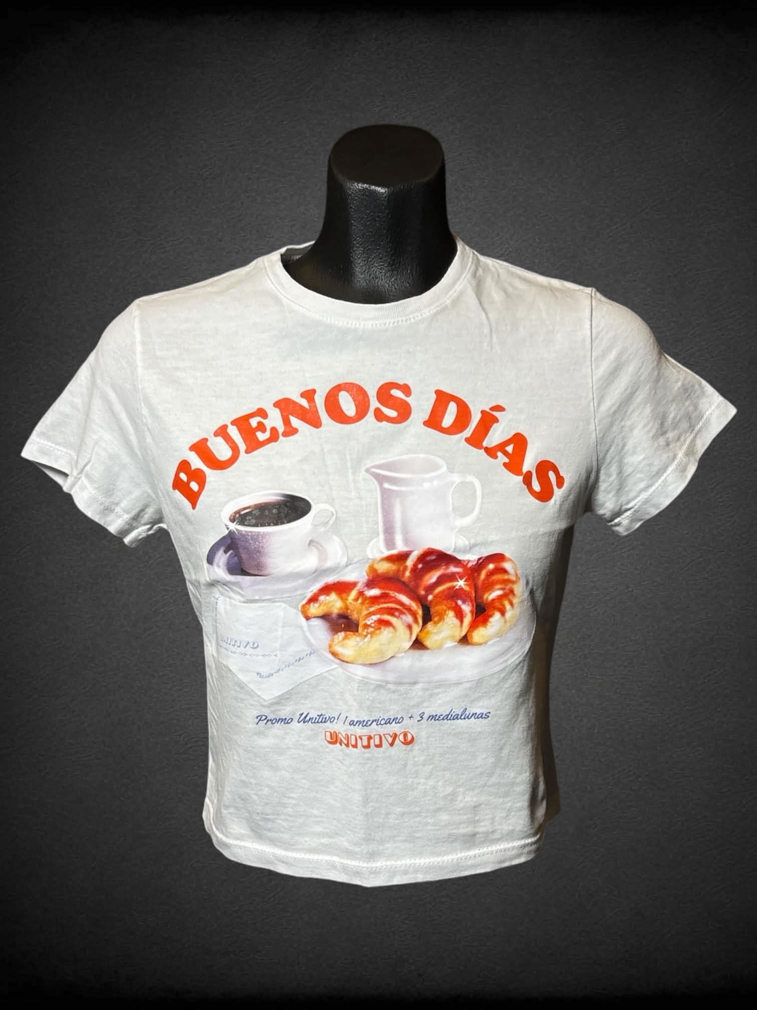 S Unitivo white cropped baby tee with breakfast “Buenos Días” graphic on front