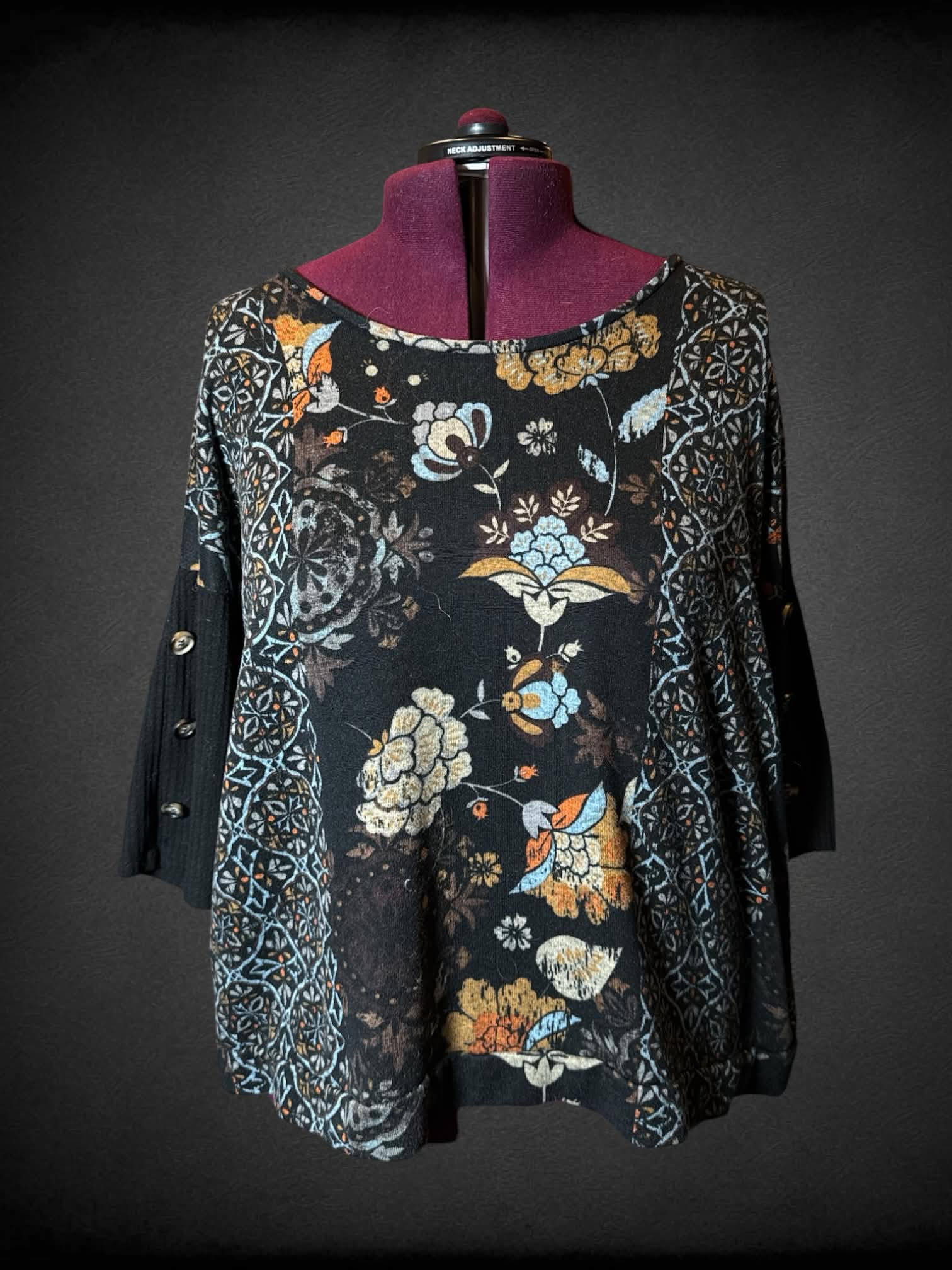 3X Notations black sweater top with colorful floral design, and decorative buttons on sleeves