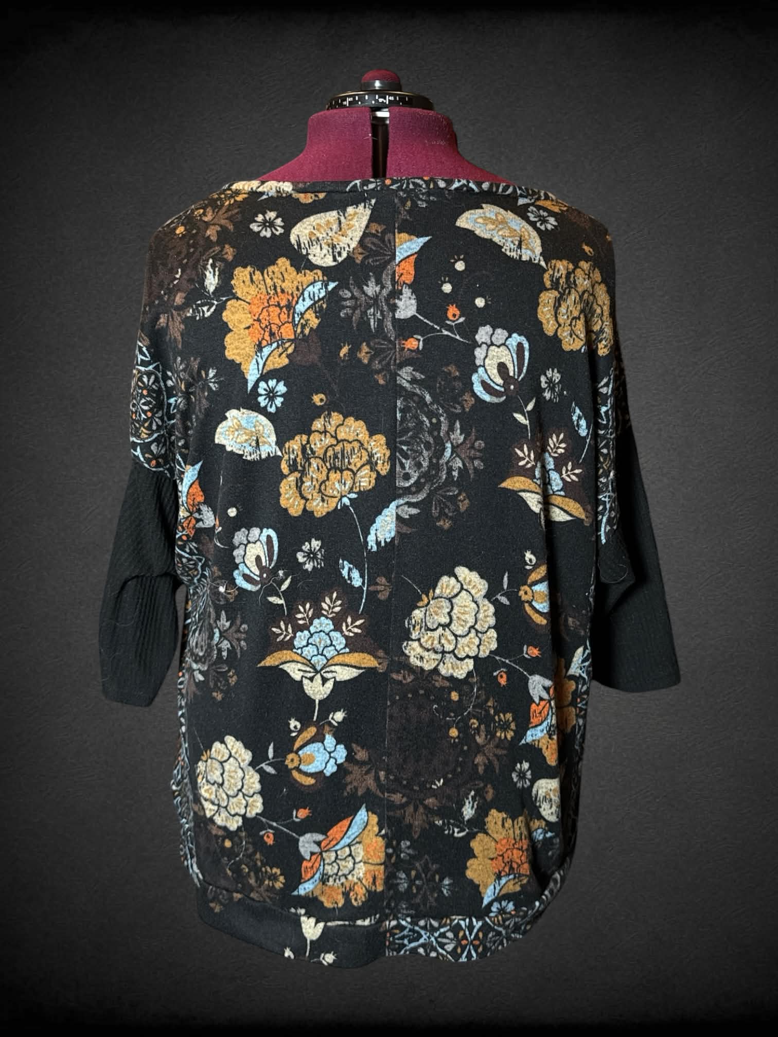 3X Notations black sweater top with colorful floral design, and decorative buttons on sleeves