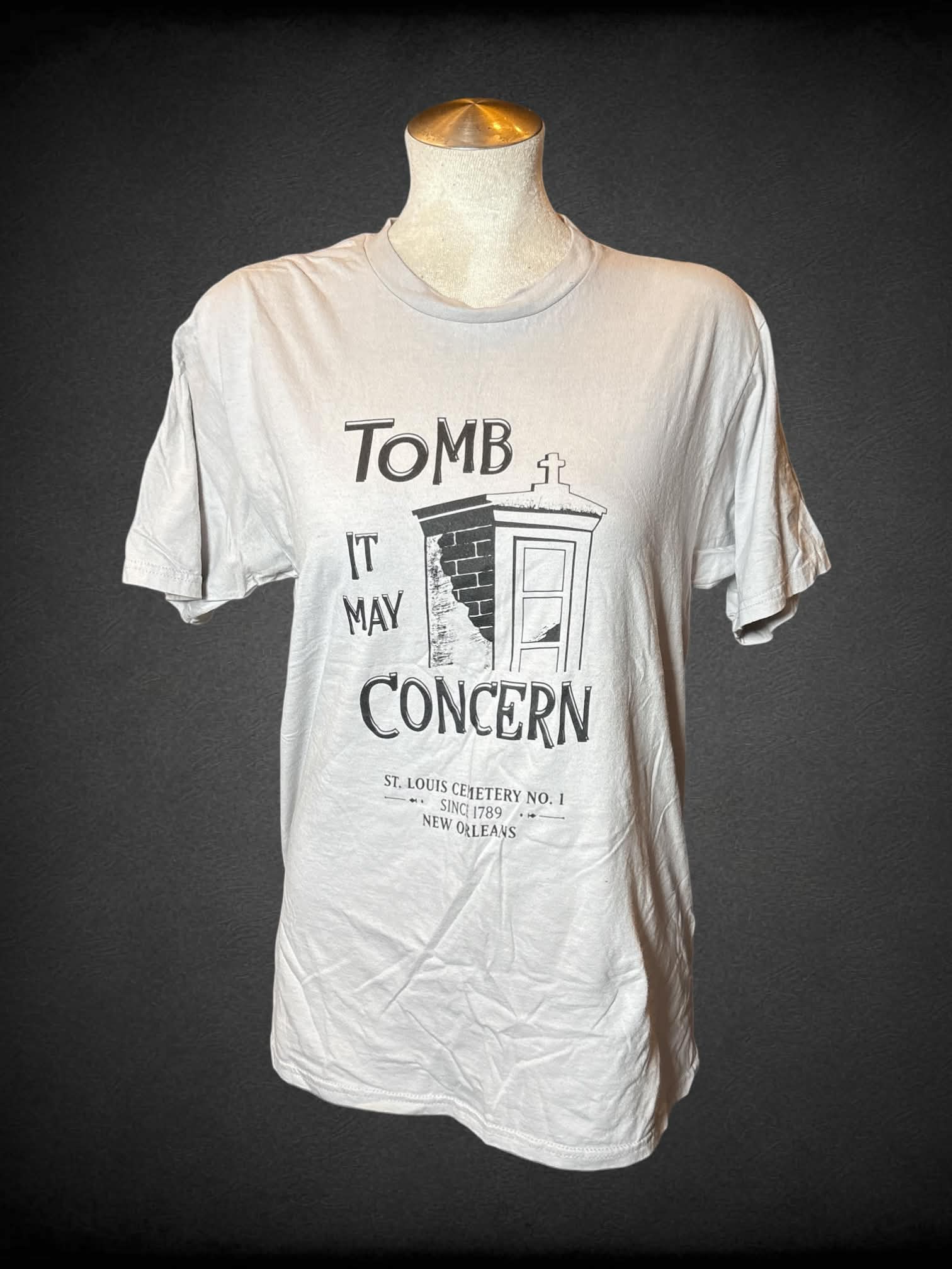 L grey t shirt with “Tomb It May Concern” writing and St. Lewis Cemetery graphic on front
