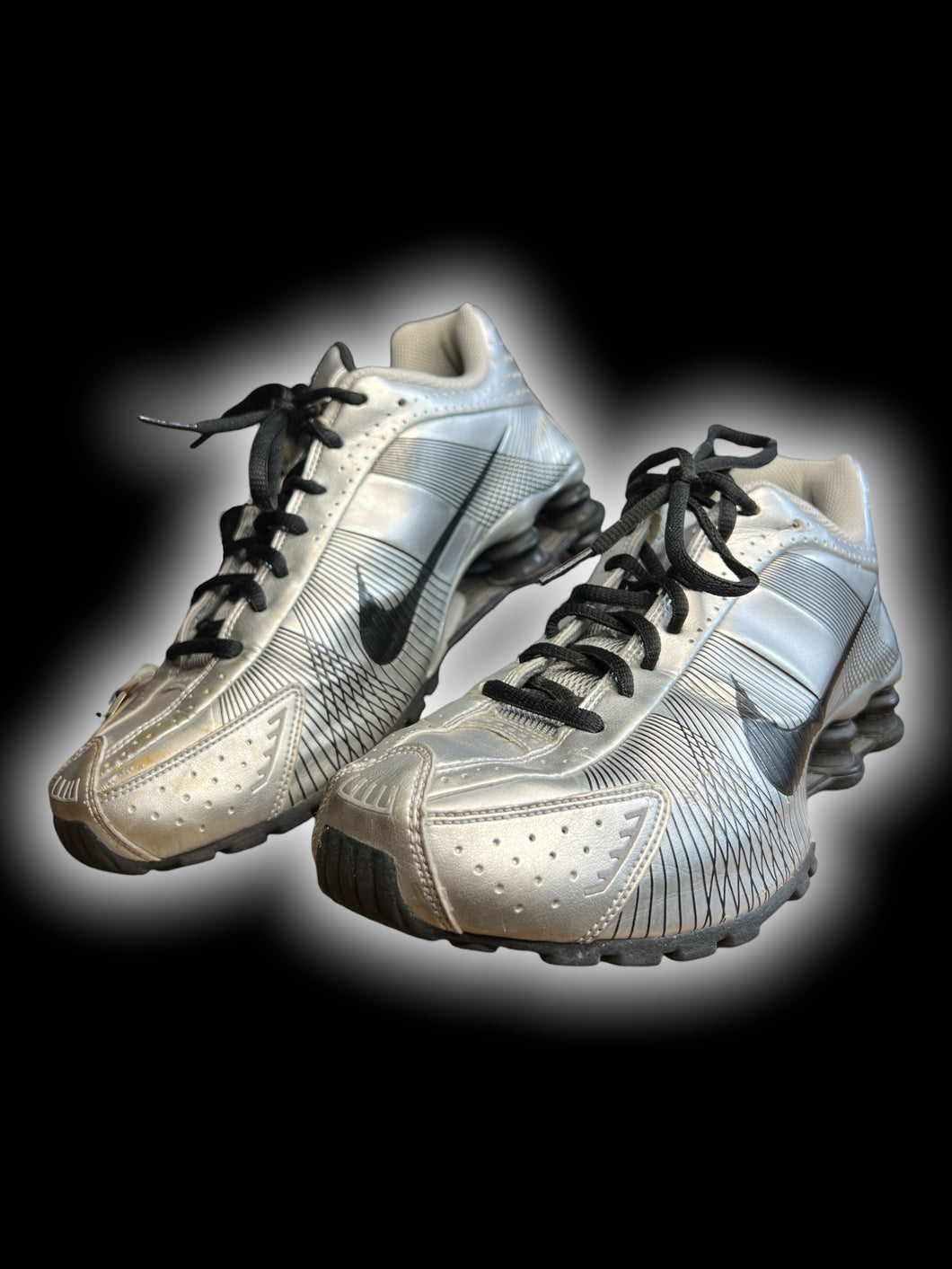 9 Silver Nike Shox sneakers w/ black geometric line pattern, black swoosh logo, black laces, shock absorber soles, & air hole perferations