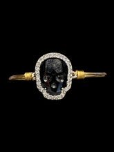 Load image into Gallery viewer, Gold like wire bracelet w black skull shaped gem, white gem outline, &amp; hook/loop closure
