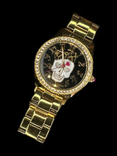 Load image into Gallery viewer, Gold-like Betsey Johnson watch w/ oyster style band, jeweled case, decorative hands, bow wearing skull face graphic, pink detail on dial, &amp; folding clasp closure
