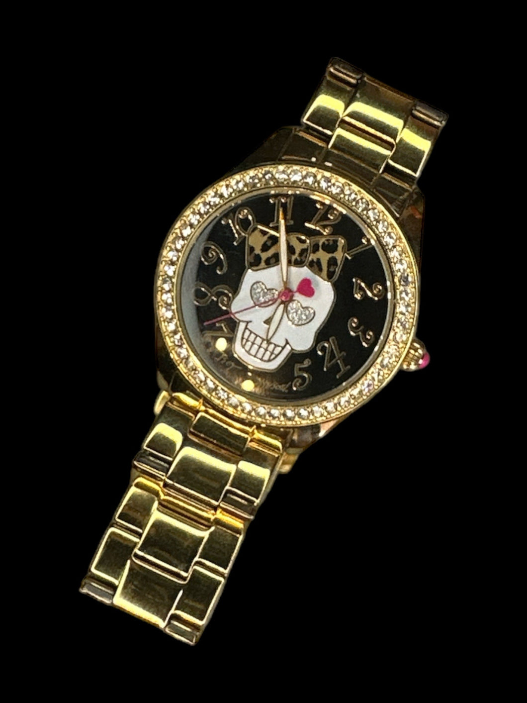 Gold-like Betsey Johnson watch w/ oyster style band, jeweled case, decorative hands, bow wearing skull face graphic, pink detail on dial, & folding clasp closure
